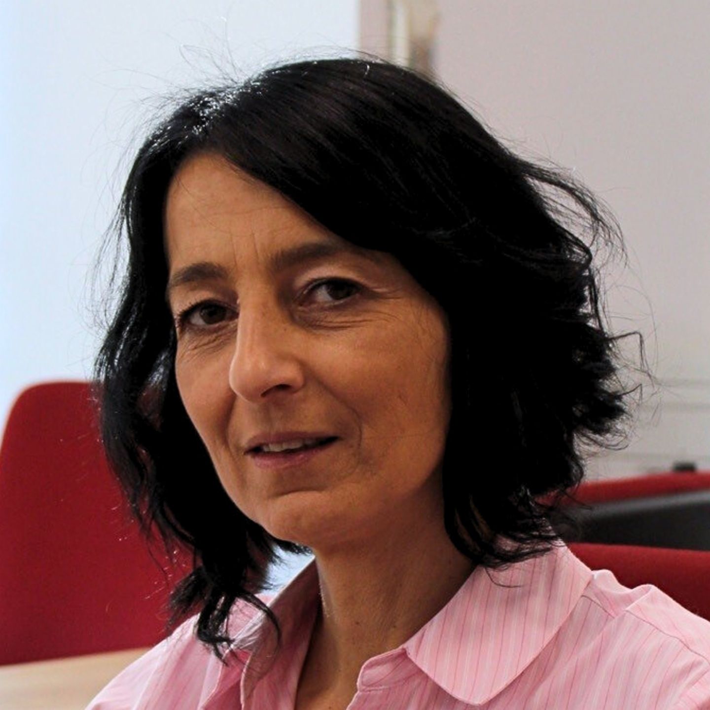 Cristina Pasere, menadžer za podršku operacijama usklađenosti u kompaniji EOS Rumunija, sedi za svojim stolom u ružičastoj prugastoj bluzi i gleda u kameru.