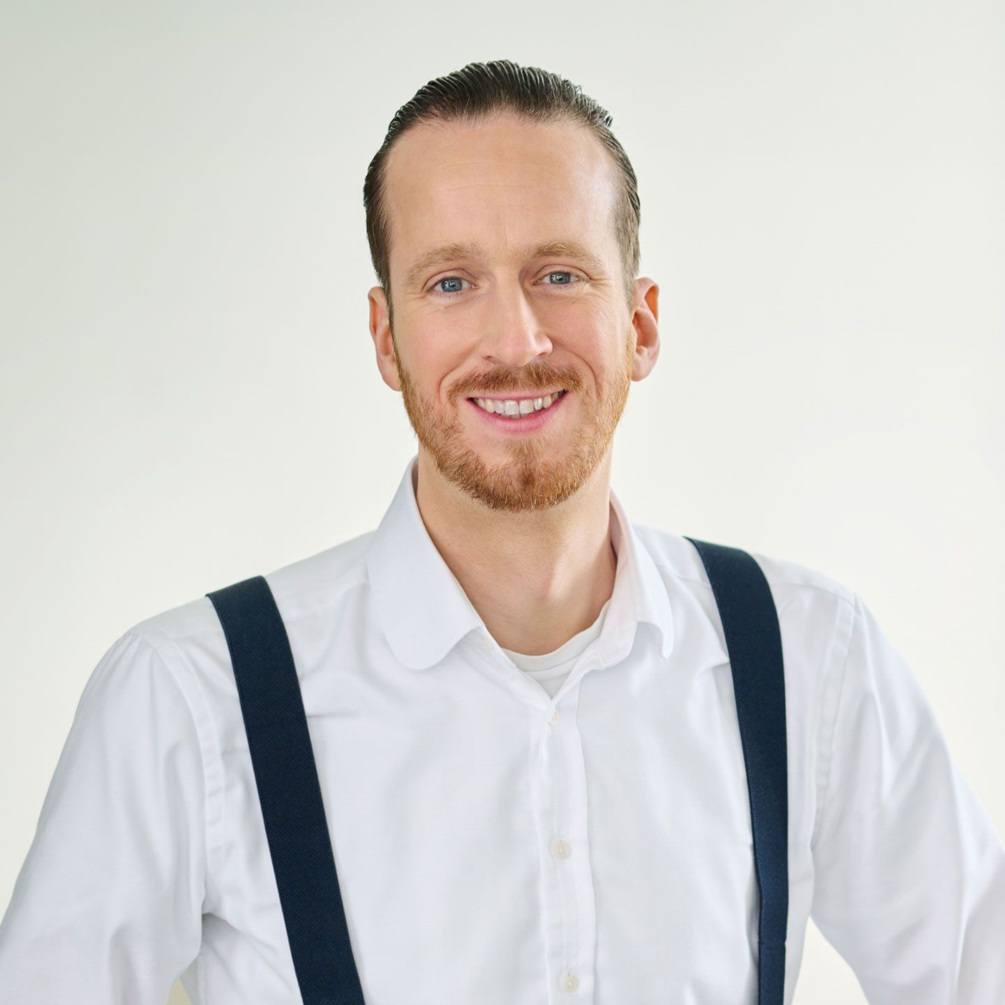 Sebastijan Polmer u beloj košulji s tregerima plave boje stoji u osvetljenoj prostoriji. 