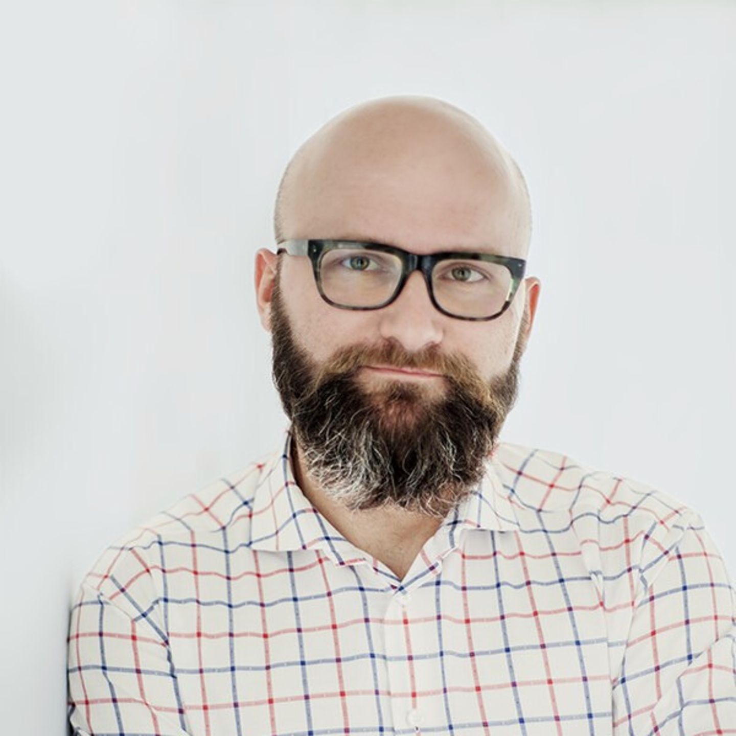 Dr. hab. Tomasz Piekot u košulji na karirane uzorke naslonjen na beli zid.