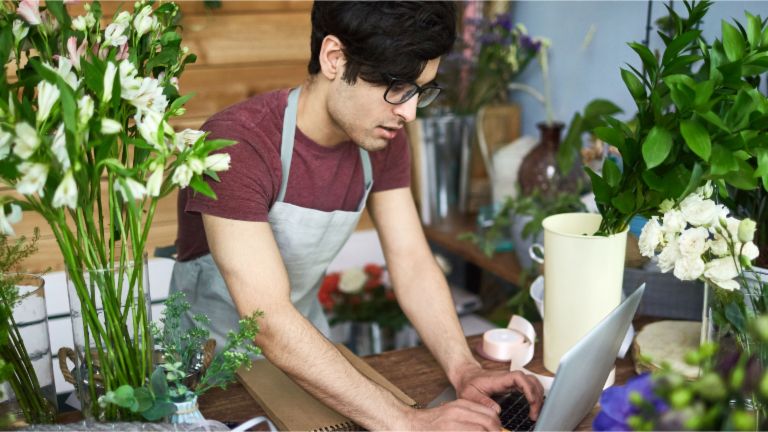 Fakturisanje: Mlad čovek u cvećari kuca na laptopu.