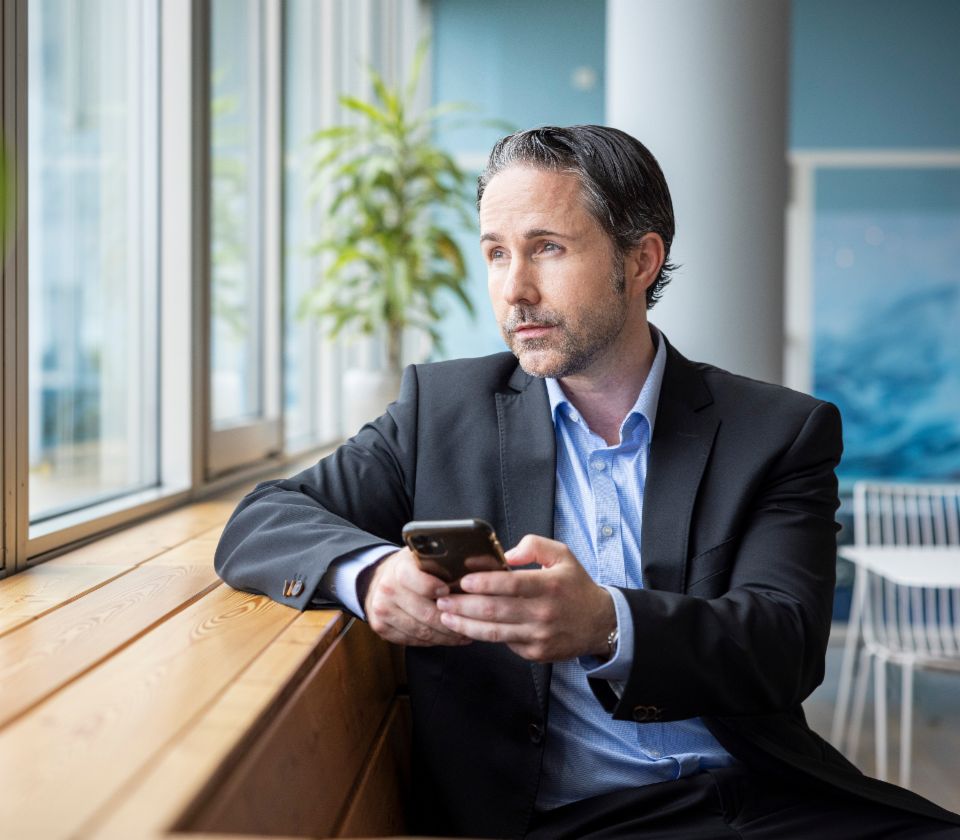 Marvin Ramke sedi na klupi i zamišljeno gleda kroz prozor. U ruci drži mobilni telefon.