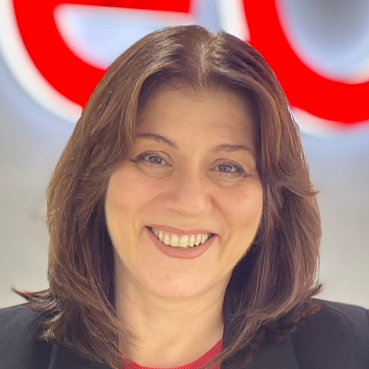 Belen Bareiro, agent kontakt centra u EOS-u u Španiji, naslanja se na pult u crnom blejzeru ispred sjajnog EOS logotipa.