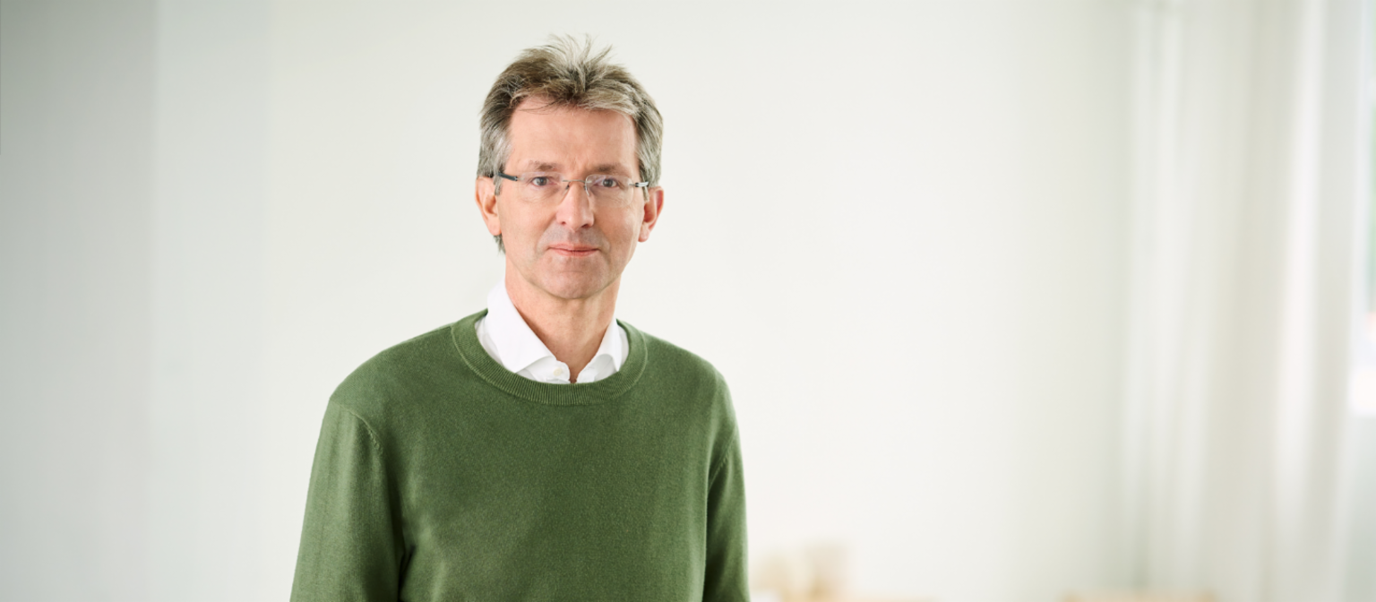 Justus Heking-Feltman, finansijski direktor, stoji u osvetljenoj prostoriji u tamnozelenom džemperu i beloj košulji.