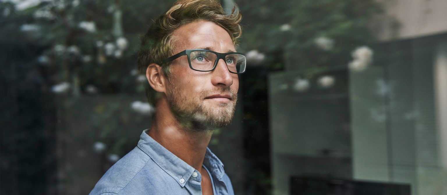 Mladi muškarac generacije Z zabrinuto viri kroz prozor.