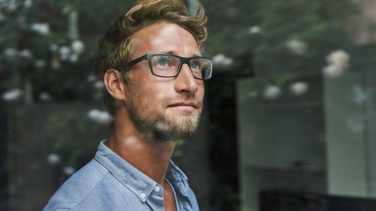 Mladi muškarac generacije Z zabrinuto viri kroz prozor.