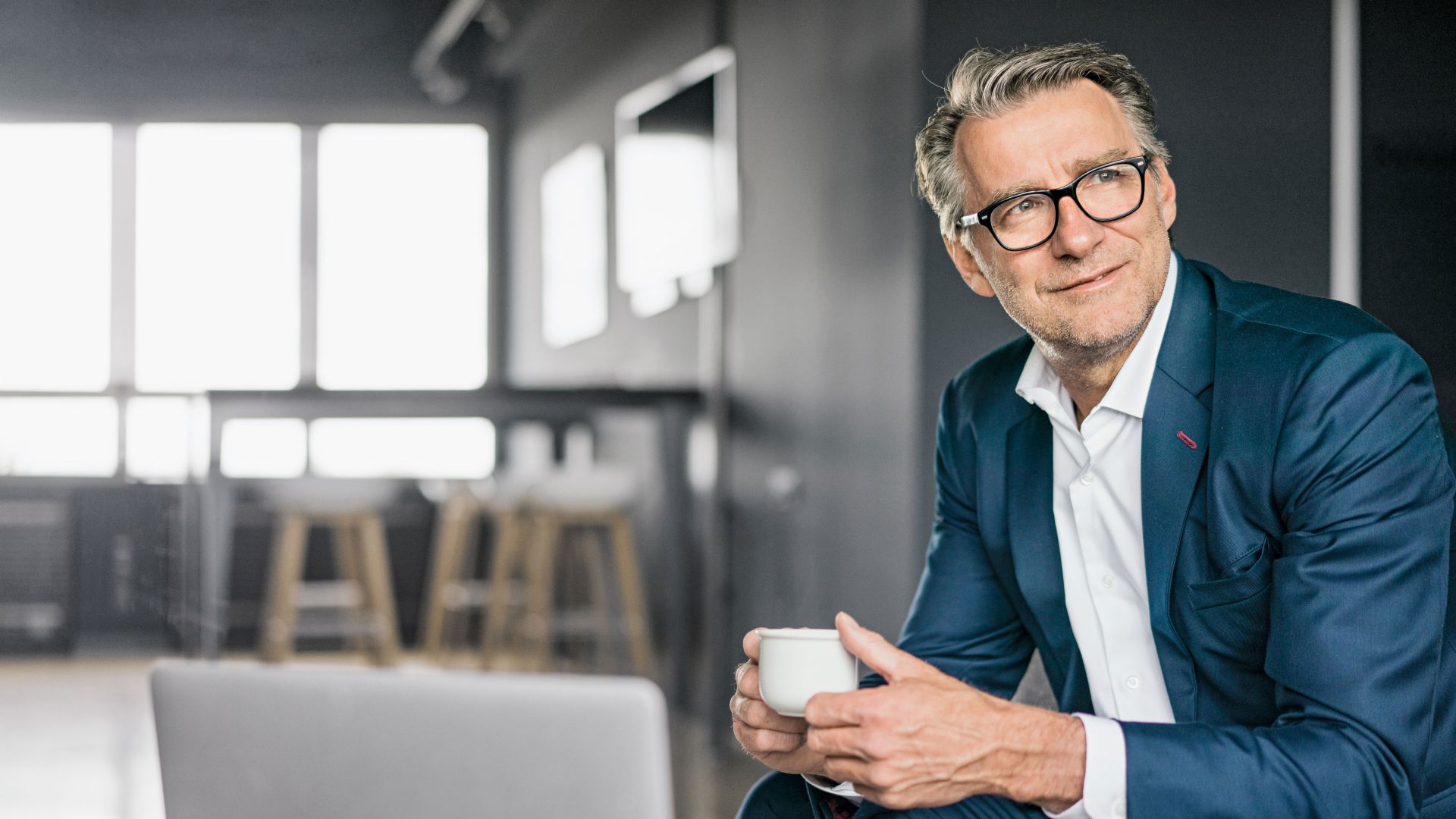 Portret zrelog poslovnog čoveka koji sedi u plavom odelu i drži belu šoljicu kafe